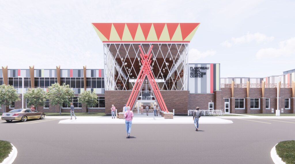 A modern building with geometric red and yellow patterns, large glass windows, and bold red structural beams at the entrance. Several people walk toward the entrance, and cars are parked nearby. Trees line the front.