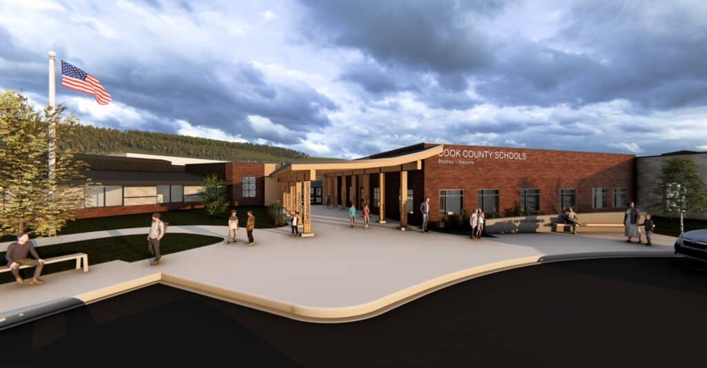 Modern school building with red brick exterior and large windows; people walk and gather outside, trees and an American flag visible, with a dramatic cloudy sky in the background.