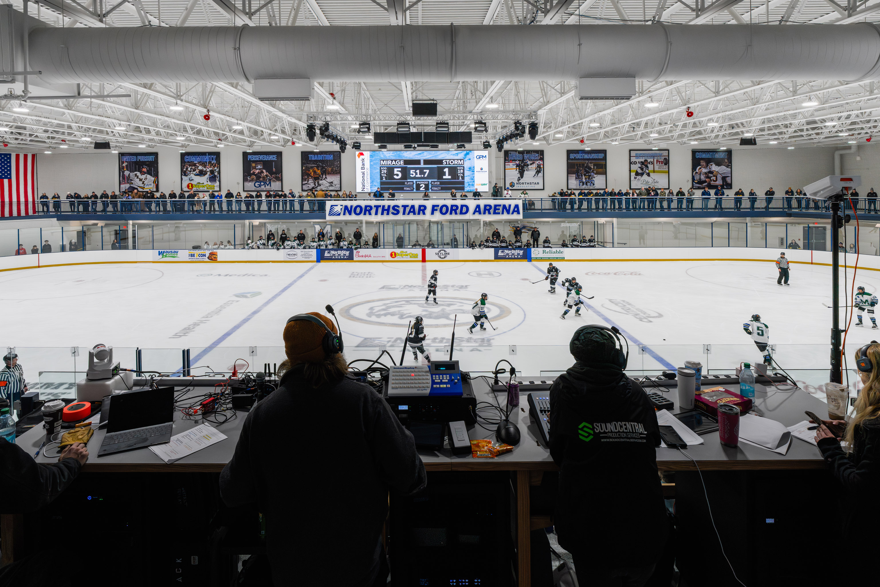 A view from the press box overlooking an ice hockey game at Northstar Ford Arena. Players are on the ice, officials and benches are visible, and people with equipment are working in the foreground.