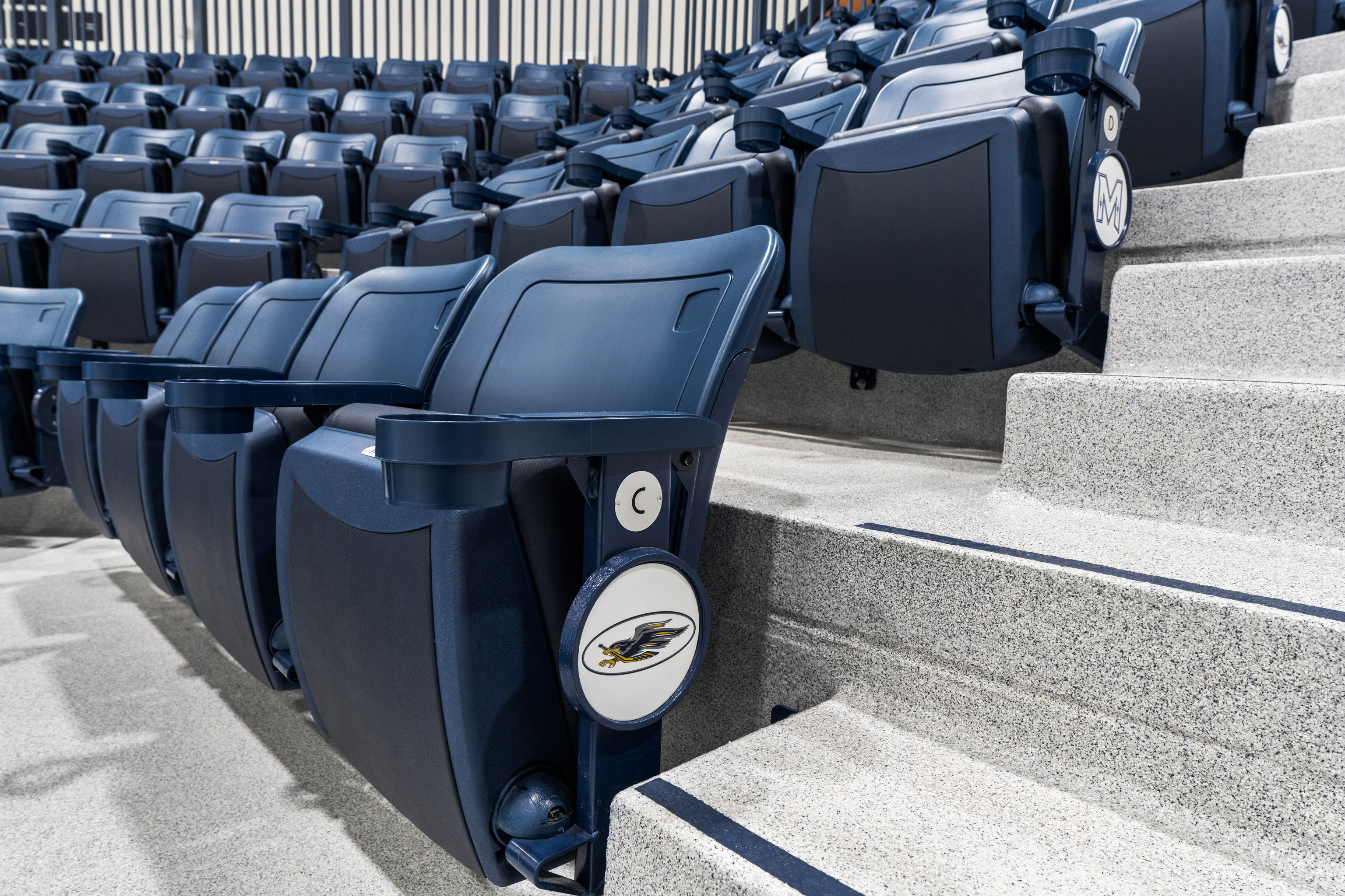 Rows of empty navy blue stadium seats next to concrete steps, each seat featuring a round logo with an eagle illustration on the side.