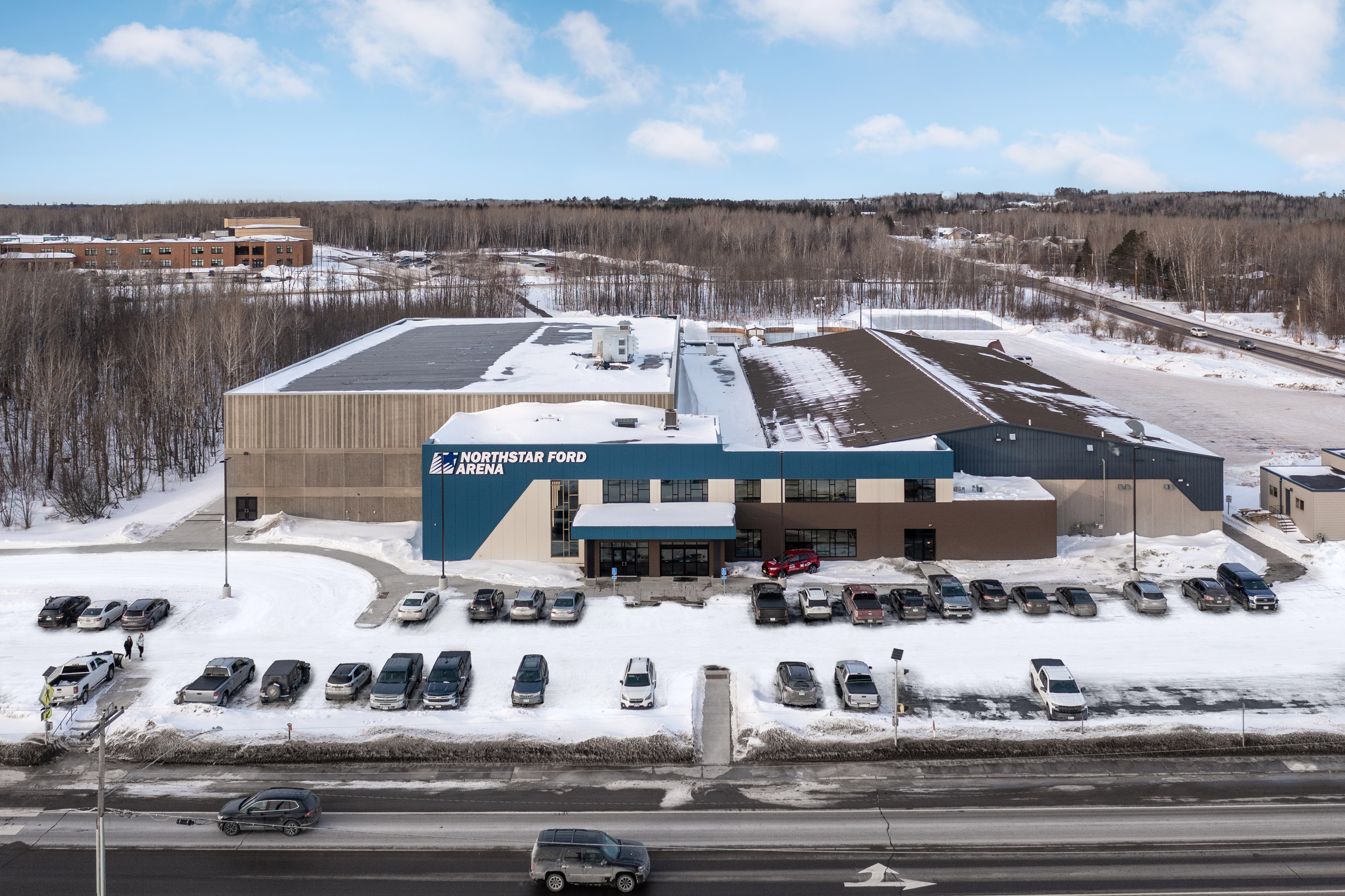 A large blue and gray building labeled "Northstar Ford Arena" sits in a snowy landscape with many cars parked in front and snow-covered trees and buildings in the background.