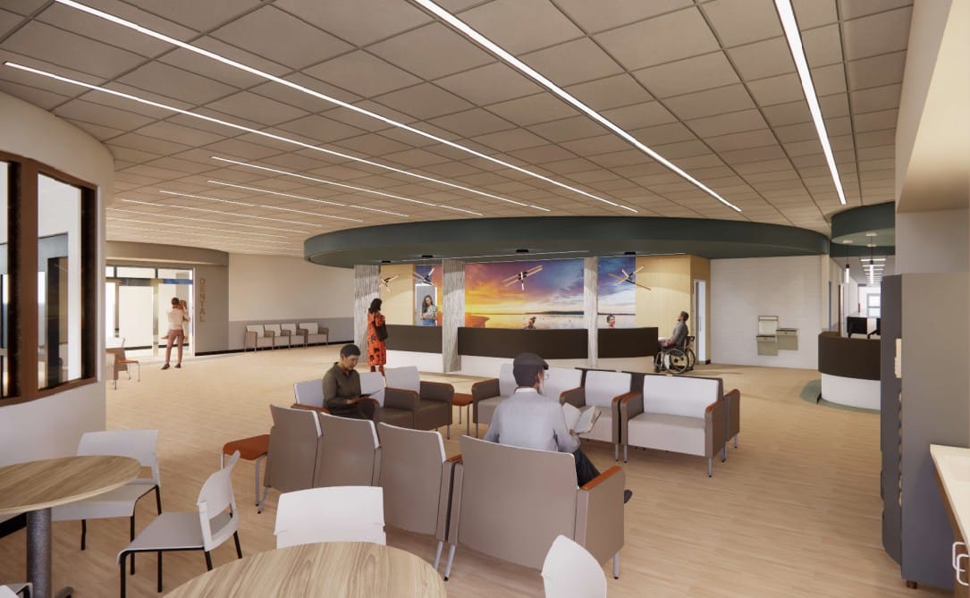 A modern waiting area with chairs, small tables, and people sitting or standing. The space features bright lighting, a mural on the back wall, and a person in a wheelchair near a reception desk.