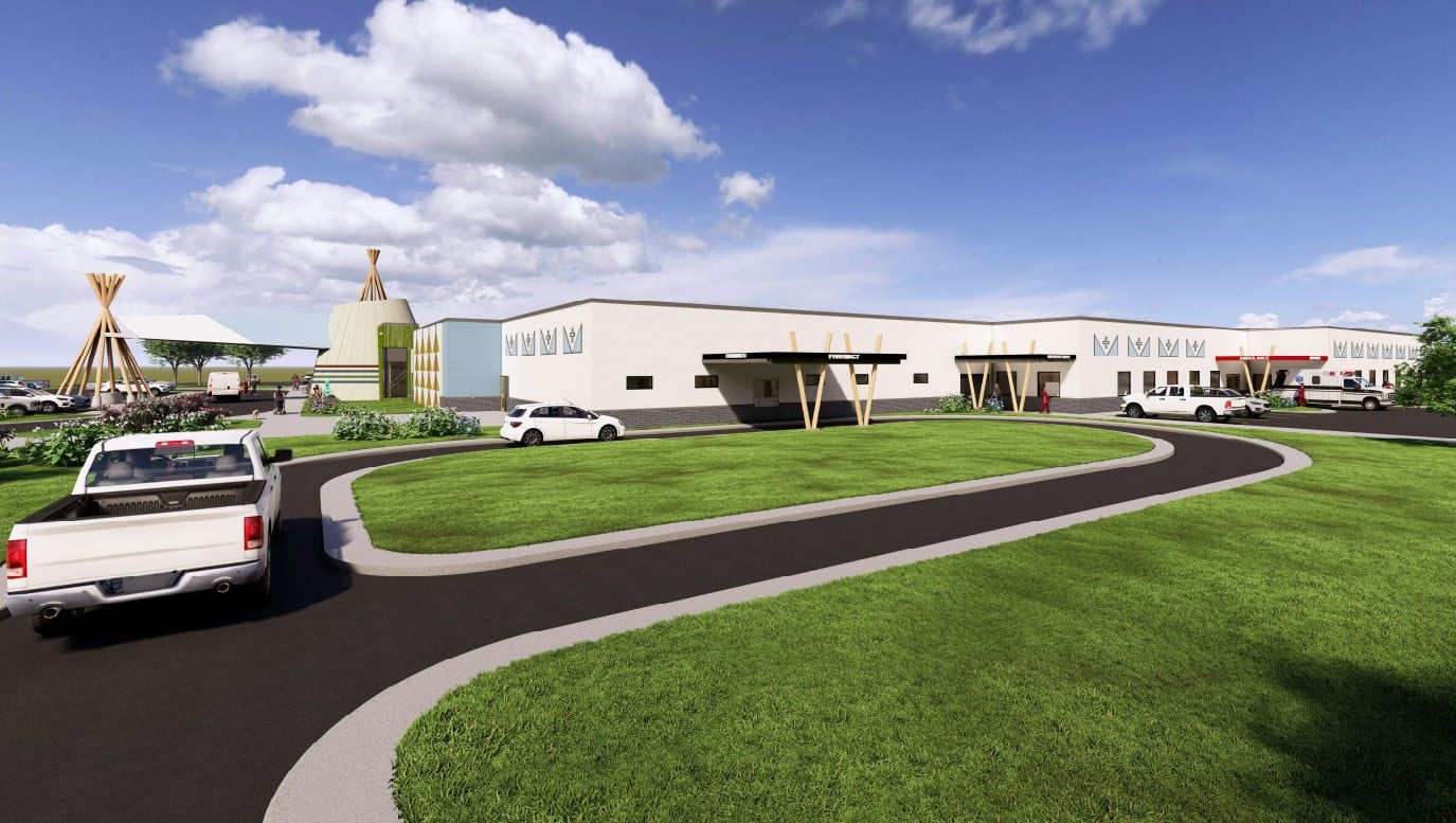 A modern, single-story building with white walls and large windows, surrounded by green grass, a circular driveway, several parked vehicles, and a few structures resembling teepees in the background under a partly cloudy sky.